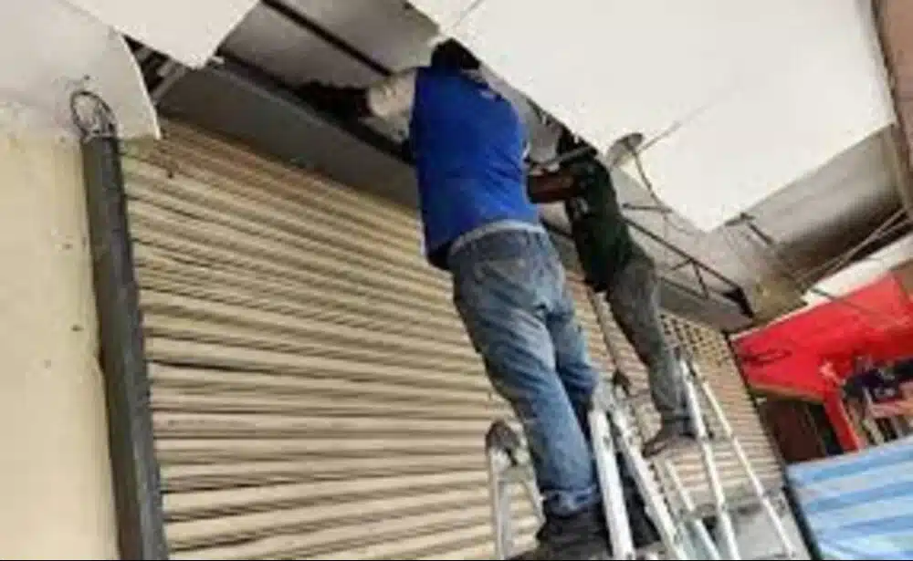 Men performing rolling shutter repair on a commercial storefront